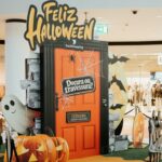 Porta cor de laranja com o letreiro “Doçura ou travessura?”, abóboras e um fantasma decorativo num centro comercial