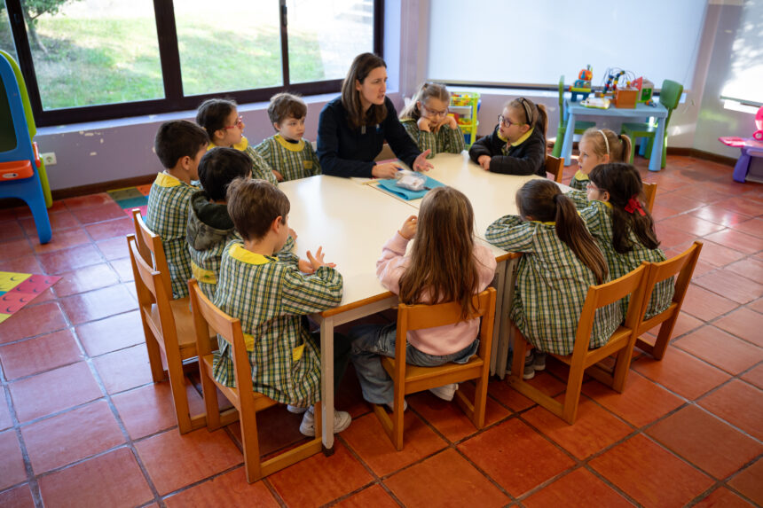 Educadora sentada a uma mesa com um grupo de crianças de bata numa sala de jardim de infância