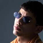 Retrato de um jovem de óculos escuros e lenço cor de laranja aos ombros, enviado pela assessoria de Genio Producer