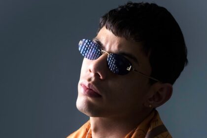Retrato de um jovem de óculos escuros e lenço cor de laranja aos ombros, enviado pela assessoria de Genio Producer