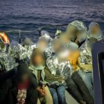 Migrantes cobertos com mantas térmicas a bordo de uma embarcação da Polícia Marítima, no mar, ao entardecer