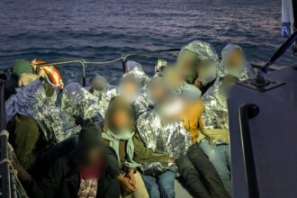 Migrantes cobertos com mantas térmicas a bordo de uma embarcação da Polícia Marítima, no mar, ao entardecer