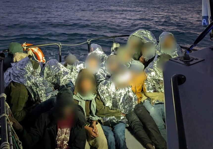 Migrantes cobertos com mantas térmicas a bordo de uma embarcação da Polícia Marítima, no mar, ao entardecer
